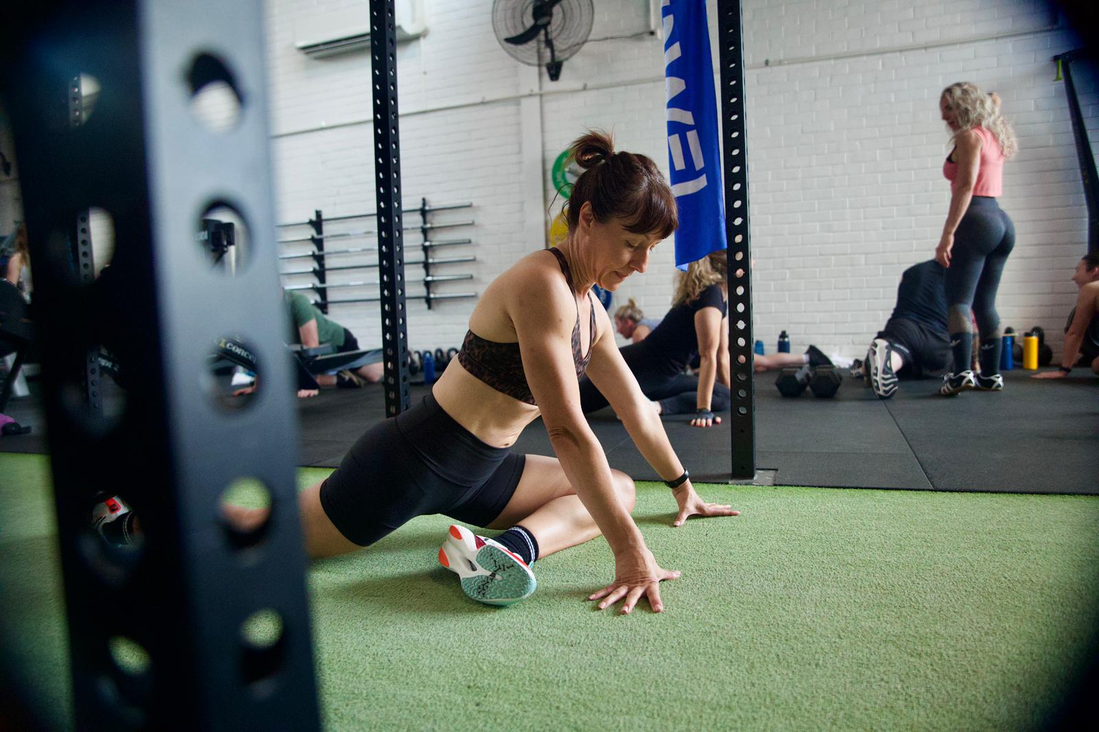 Member performing focused mobility work on the turf, framed through squat rig uprights