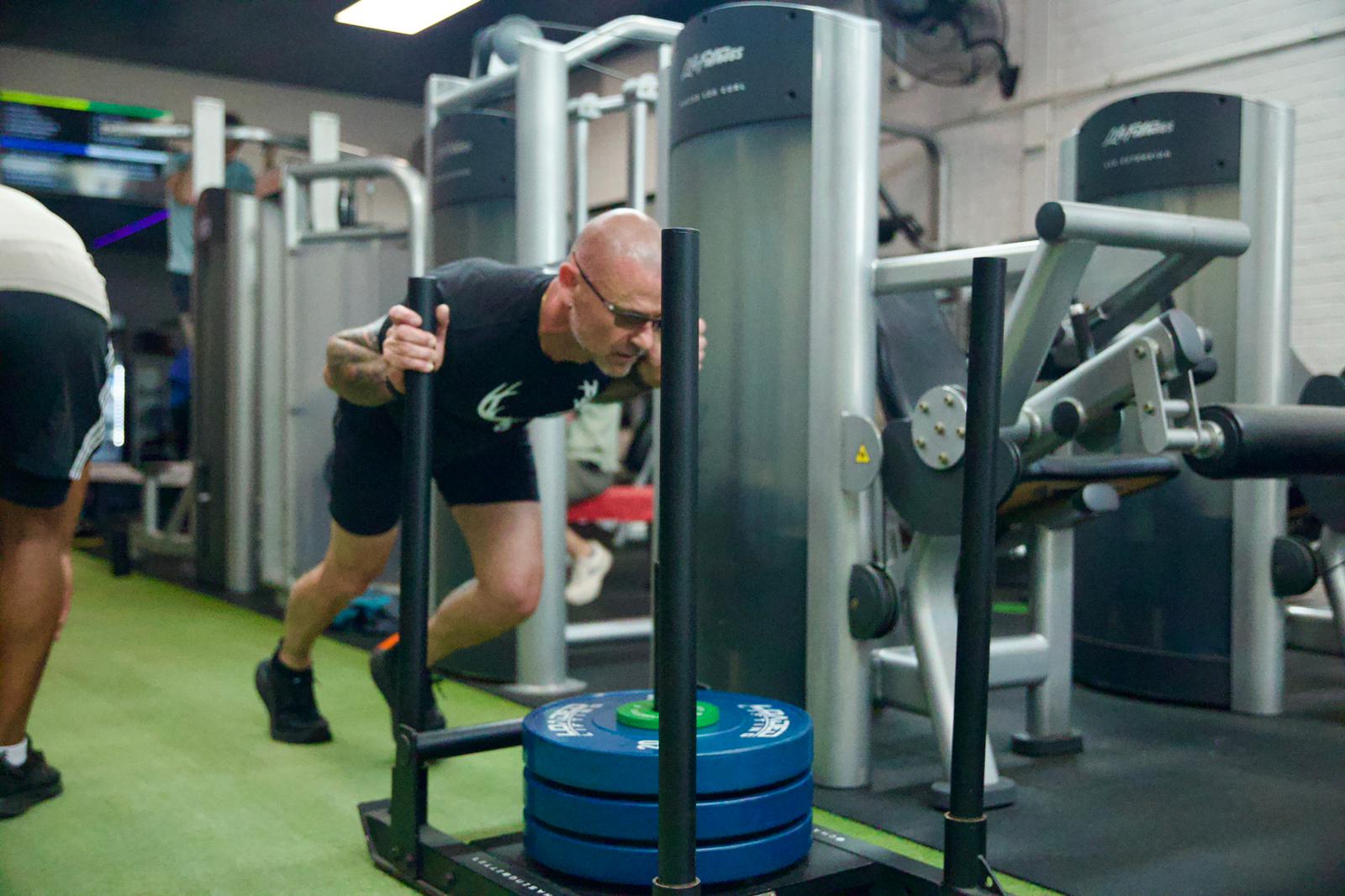 Member driving a weighted sled across the turf during strength training